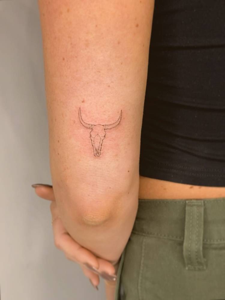Bull skull tattoo located on the tricep, done in fine line style.