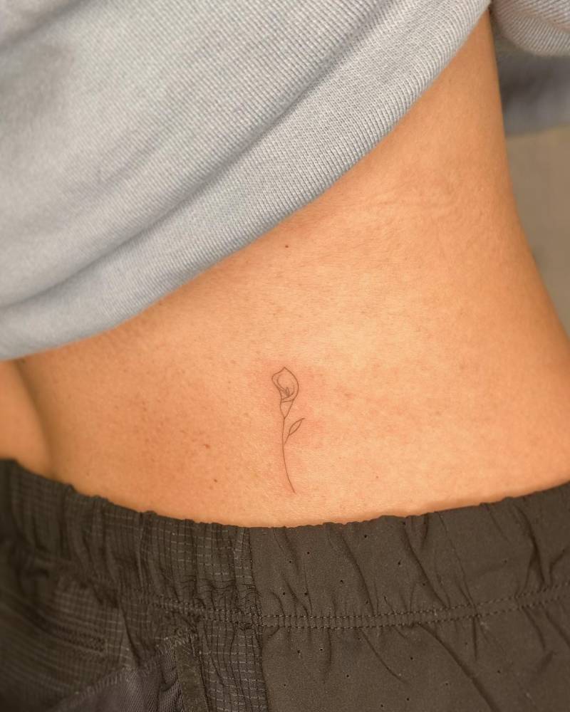 Calla lily flower tattooed on the lower back, fine line style.