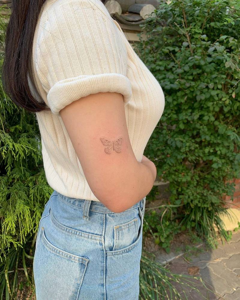 Hand poked fine butterfly tattoo located on the upper arm.