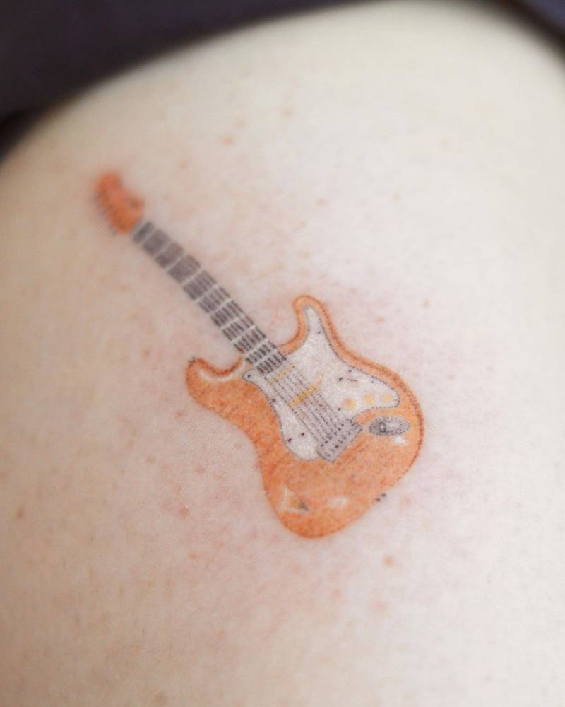 Hand poked guitar tattoo located on the upper arm.