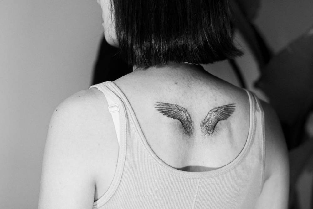 Micro-realistic style wings tattoo located on the upper back.