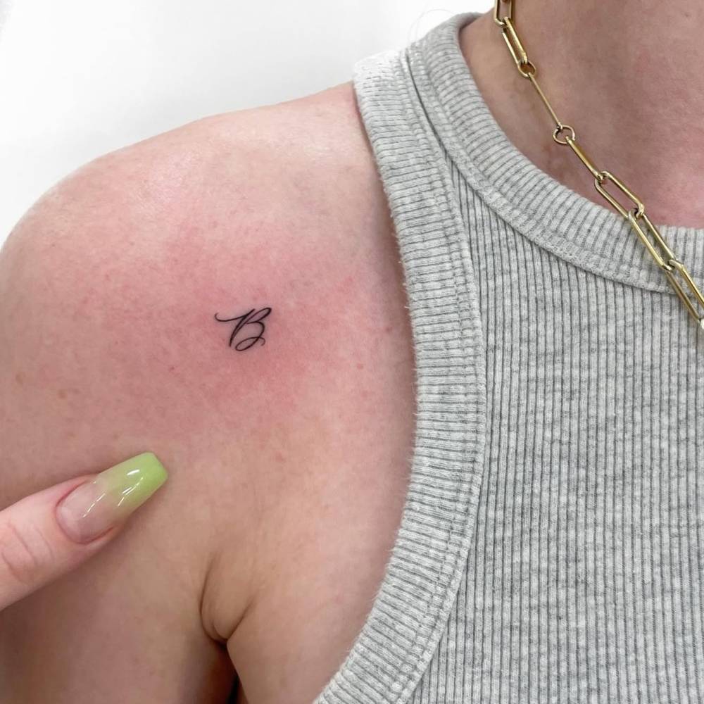 Tattoo of the letter "B" in script font located on the shoulder.