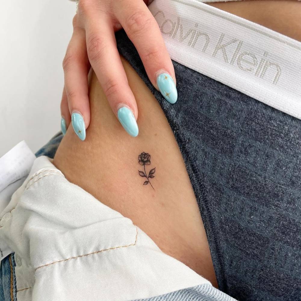 Tiny rose tattoo placed on the pelvis, done in illustrative style.