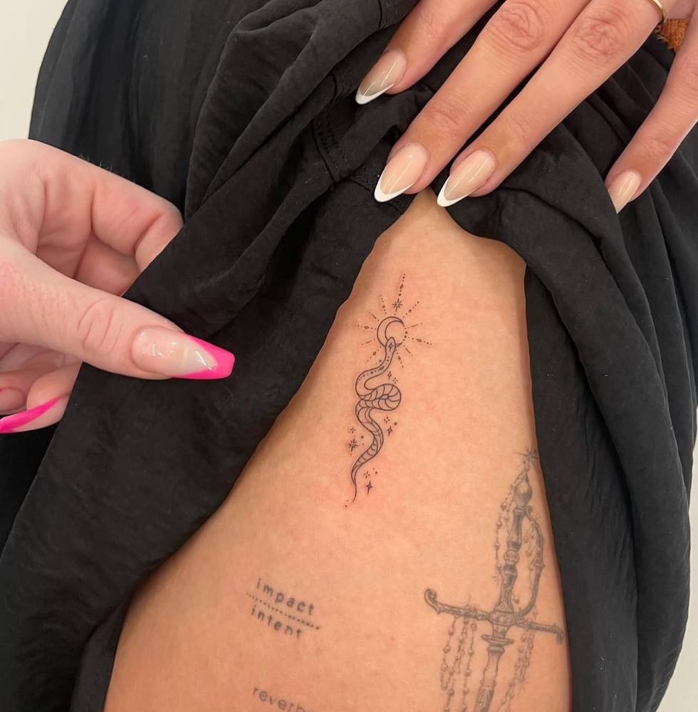 Snake and crescent moon tattoo located on the thigh, fine line style.