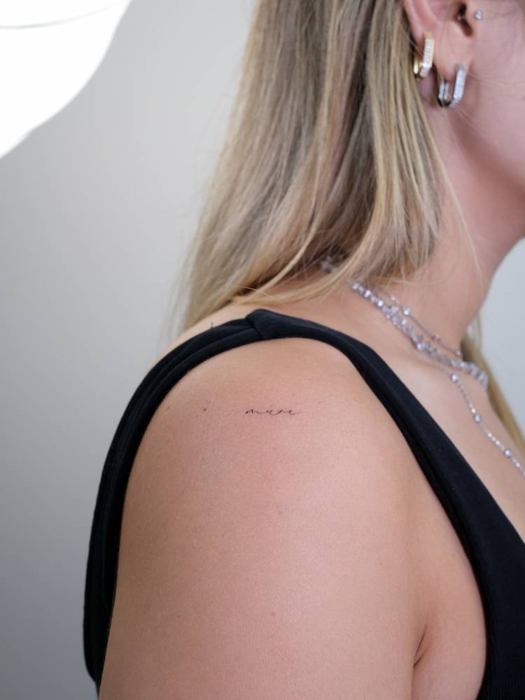 Tiny lettering tattoo of the word "muse" located on the shoulder.