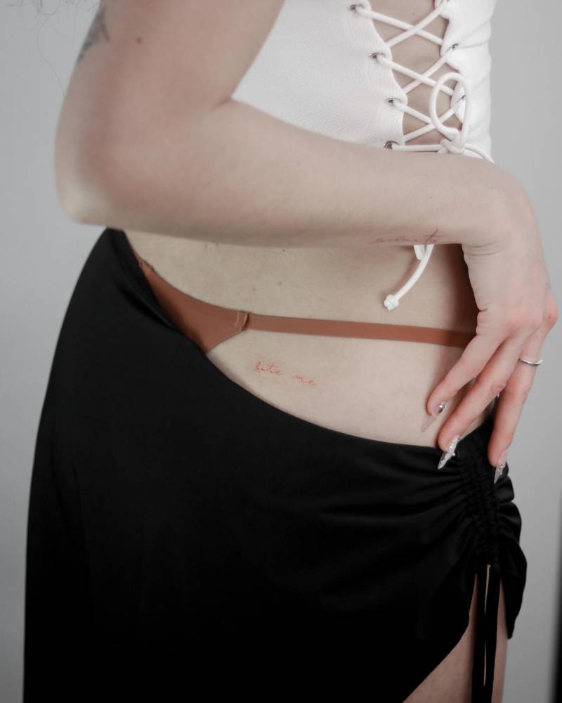 "Bite me" lettering tattoo in red ink located on the butt cheek.
