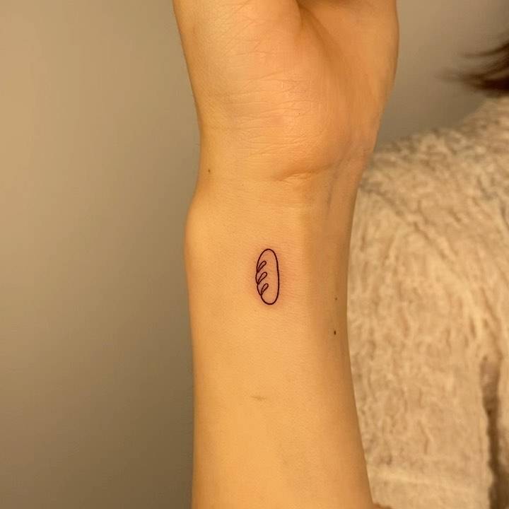One line bread tattoo located on the wrist, minimalistic style.