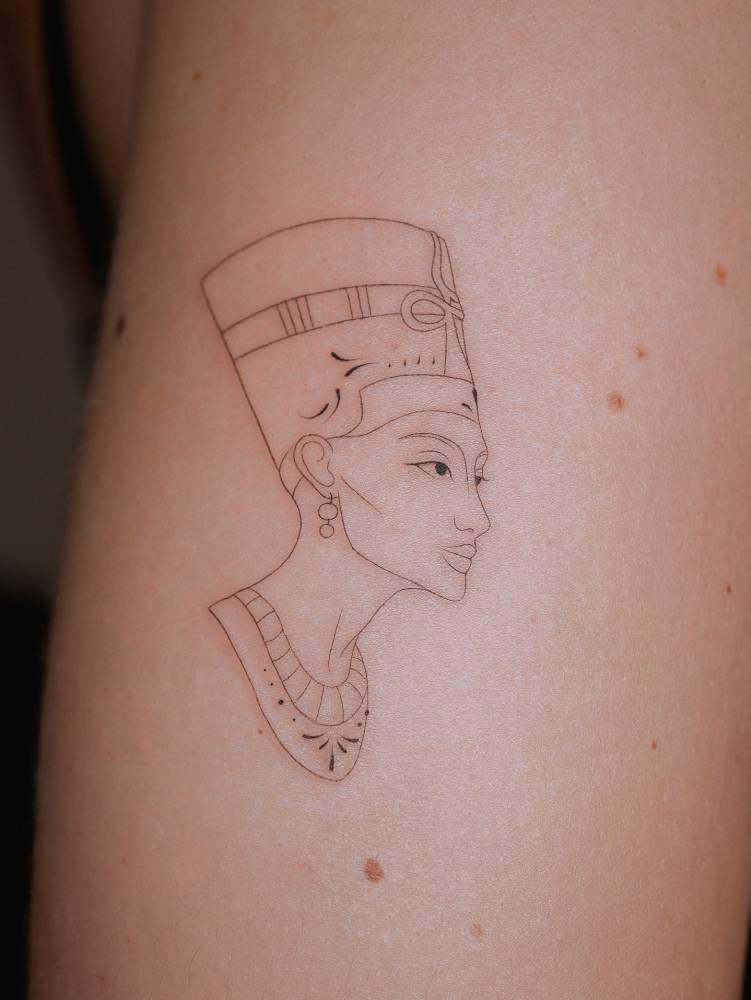 Nefertiti portrait tattoo in fine line style done on the upper arm.
