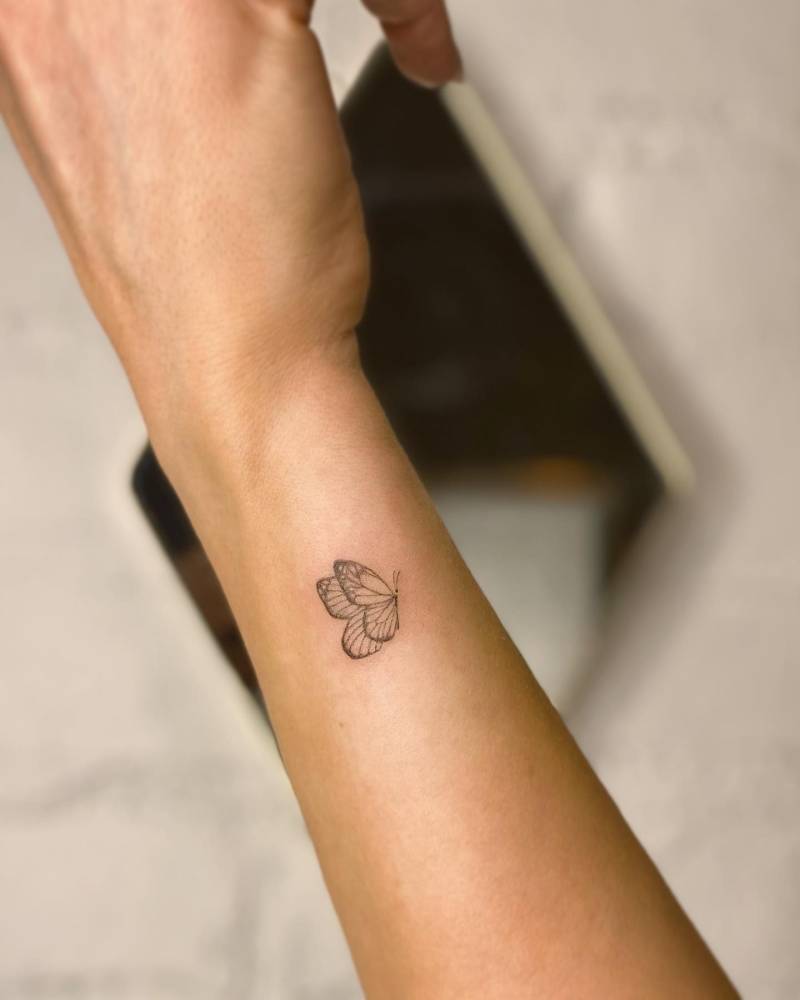 Little butterfly tattoo in illustrative style located on the wrist.