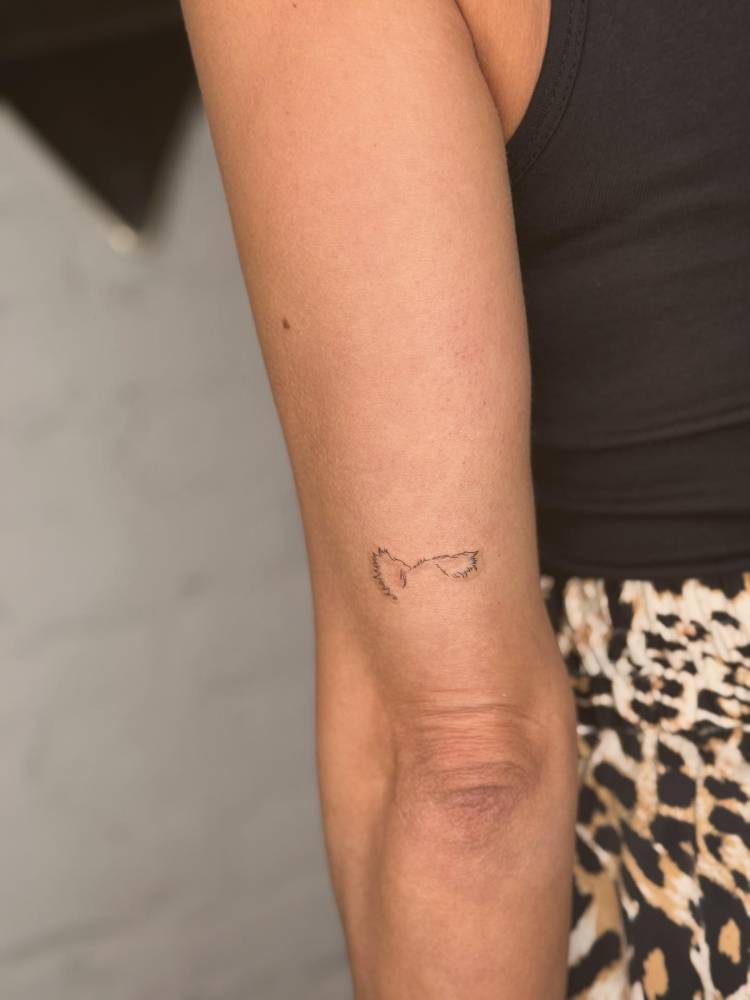 Dog ears tattoo located on the tricep, done in fine line style.