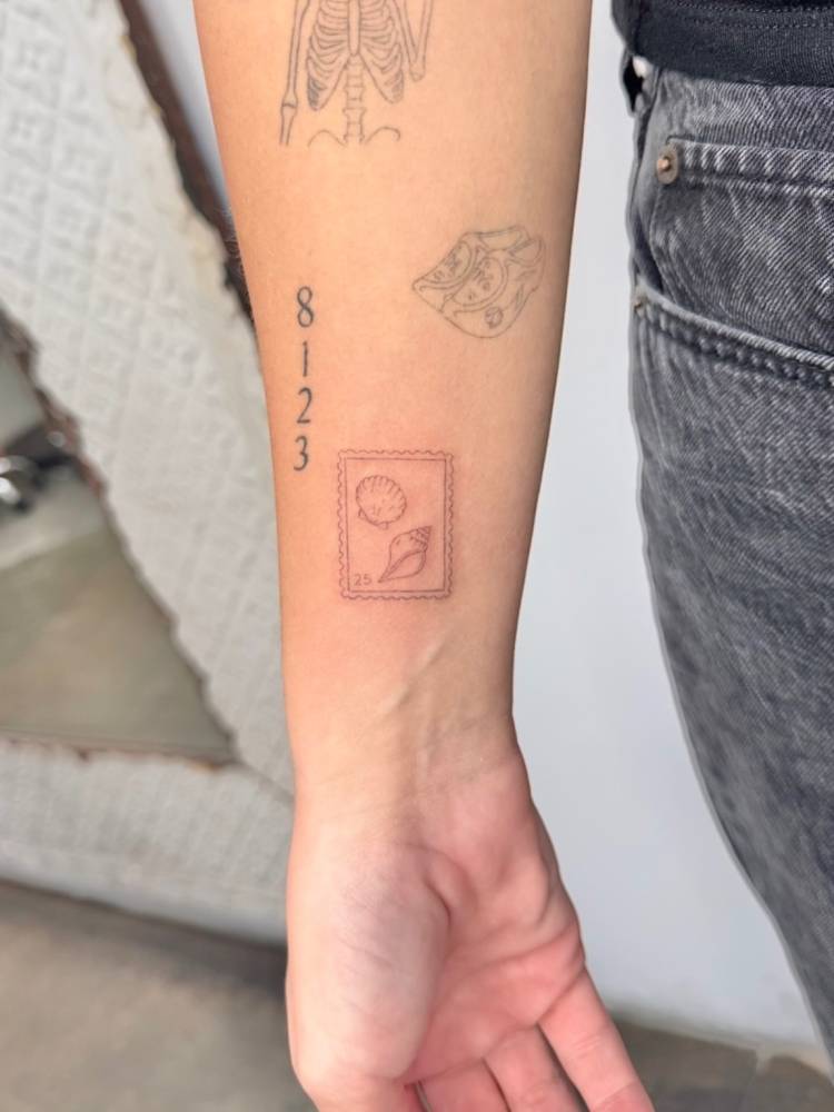 Shells stamp tattoo in fine line style placed on the wrist.