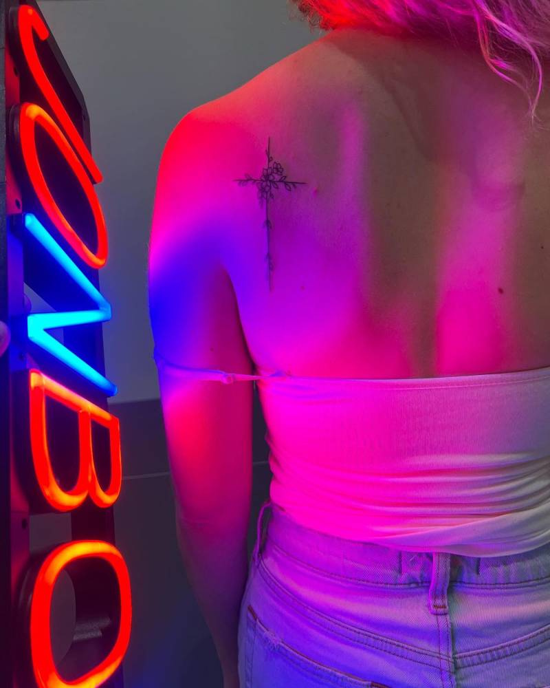 Flower cross tattoo located on the shoulder blade, illustrative style.