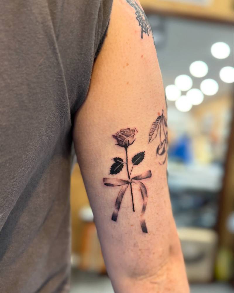 Rose and ribbon tattoo located on the tricep, done in illustrative style.