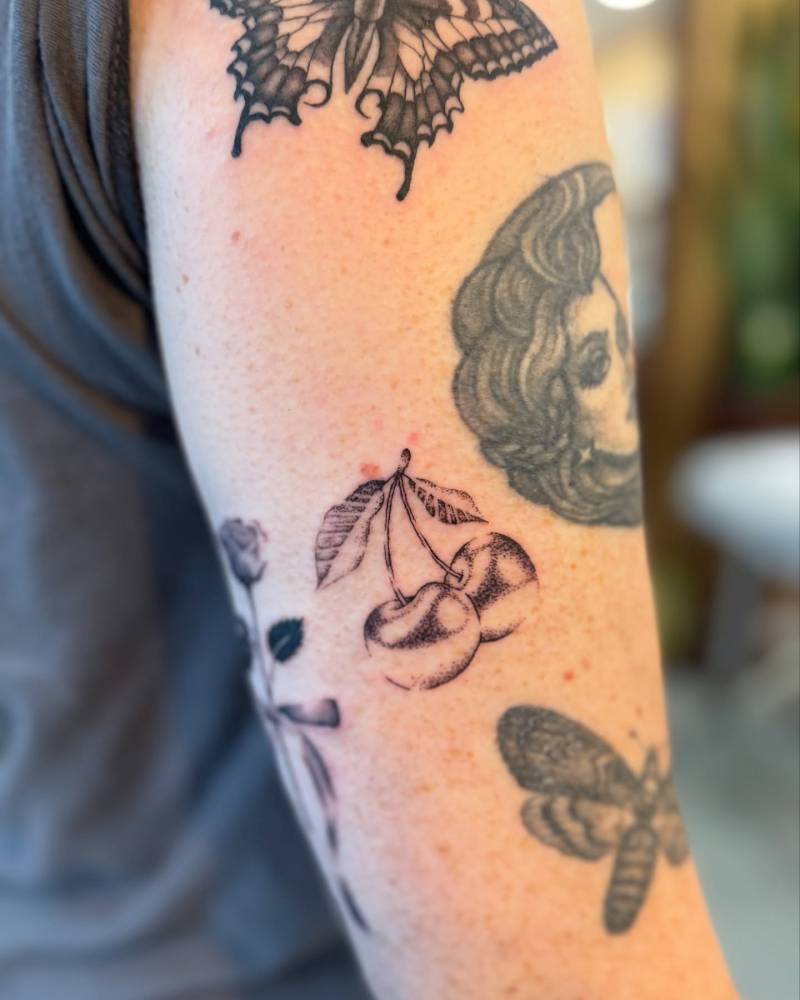 Metallic effect cherries tattooed on the upper arm.