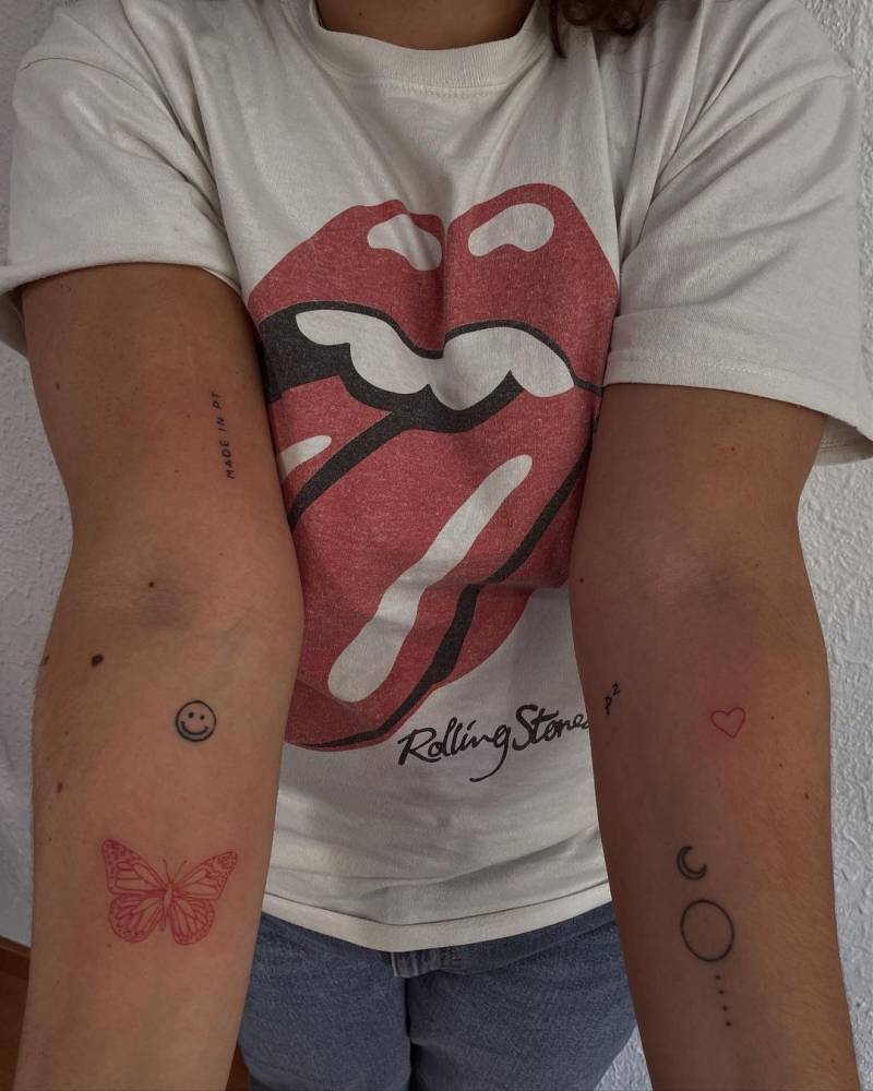 Red butterfly and red heart tattoos on the inner forearm.