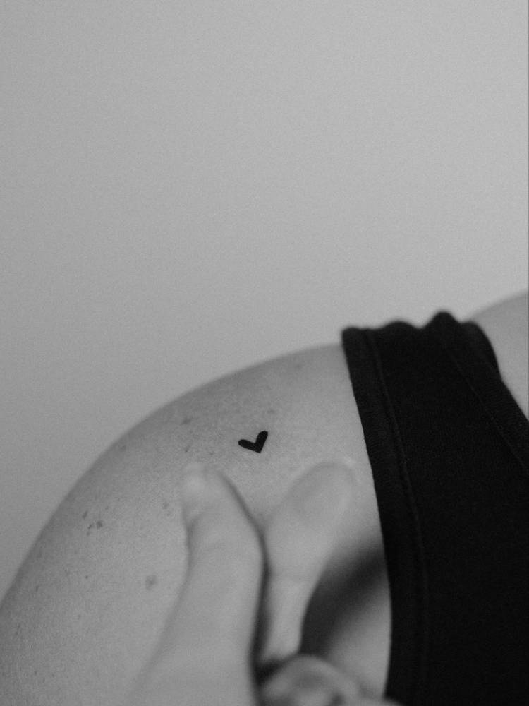 Tiny minimalistic black heart tattooed on the shoulder.