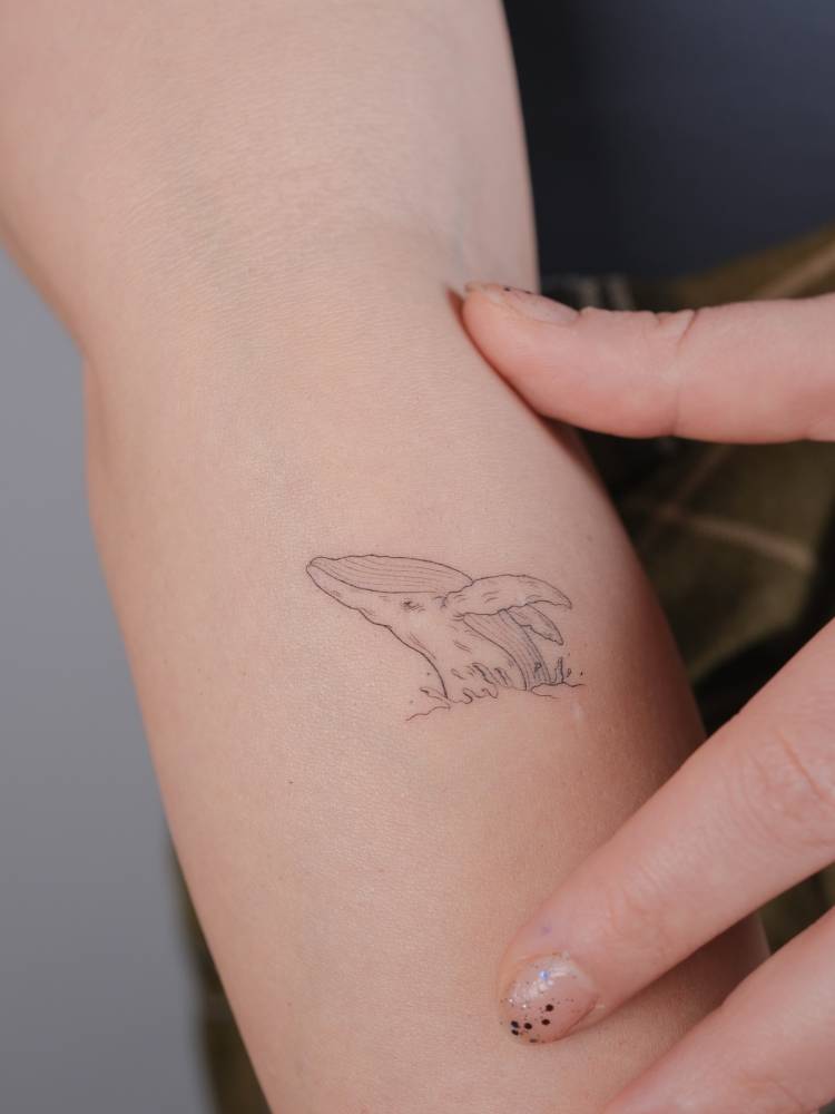 Whale tattoo in fine line style located on the forearm.