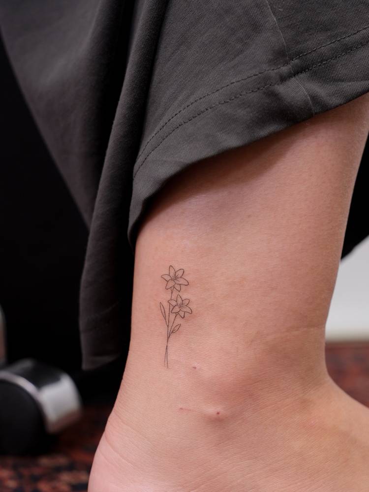 Fine line style lily flowers tattoo placed on the ankle.