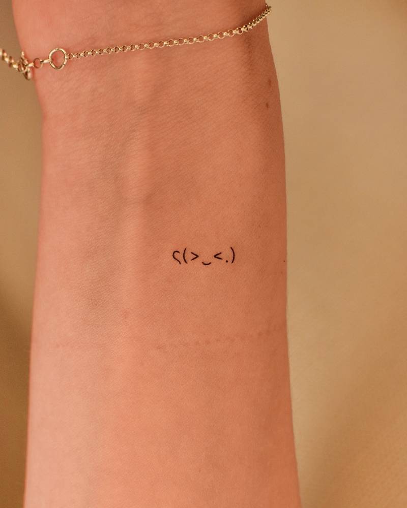 Tiny minimalistic emoji face tattooed on the wrist.