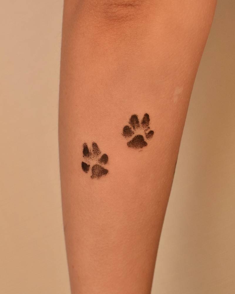 Watercolor style dog paw prints tattooed on the forearm.