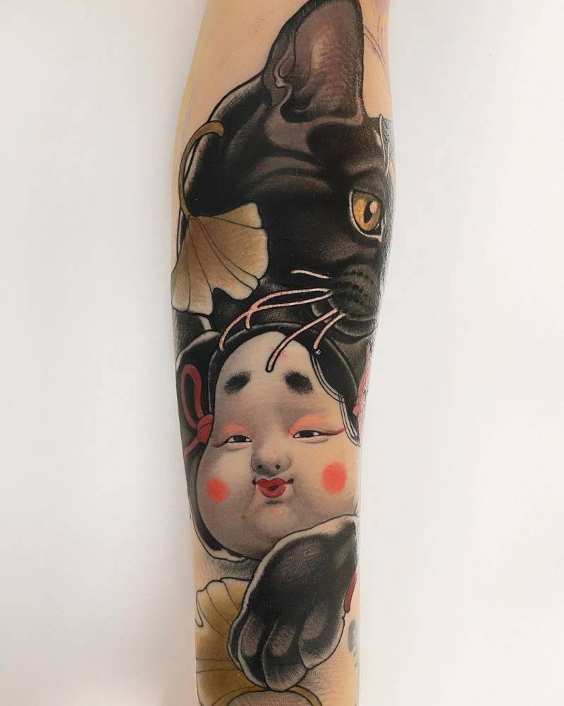 Okame mask and black cat tattoo on the inner forearm