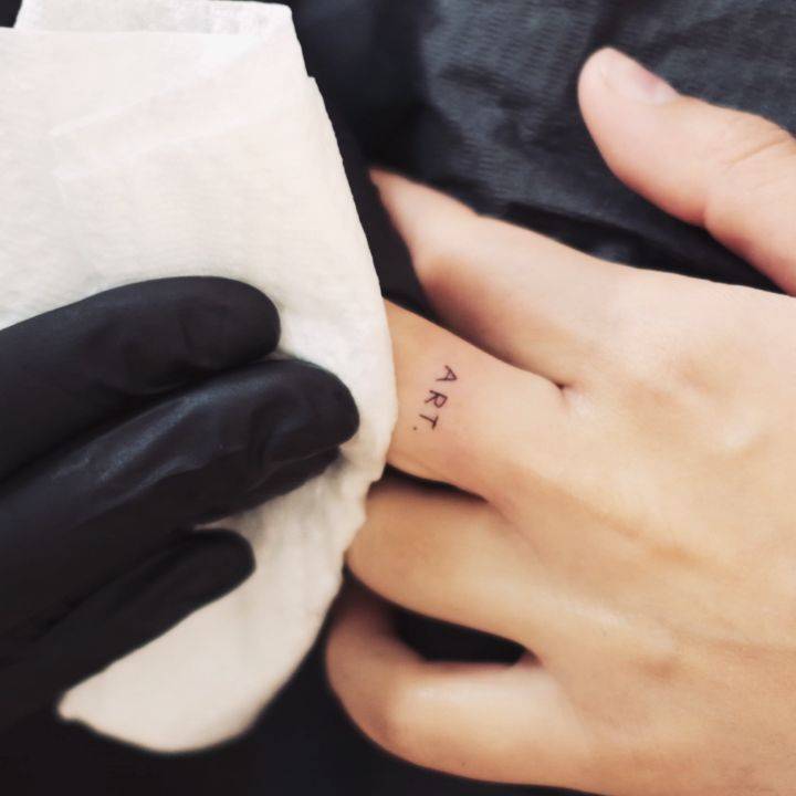 Tattoo of the word "art" handwritten on the finger.