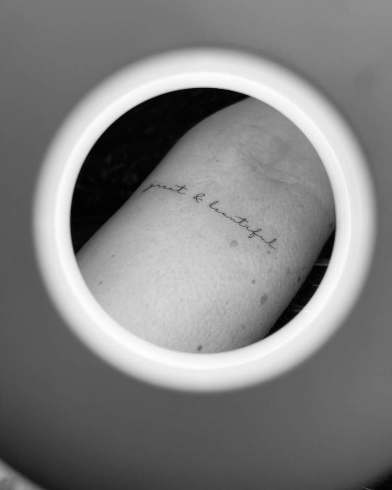 Lettering tattoo that says "great and beautiful" handwritten on the inner forearm.