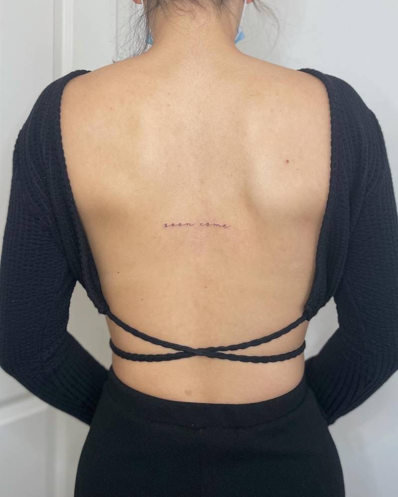 Lettering tattoo that says "soon come" located on the back.