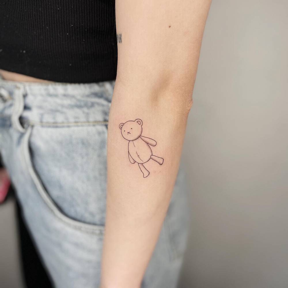 Fine line teddy bear tattoo located on the forearm.