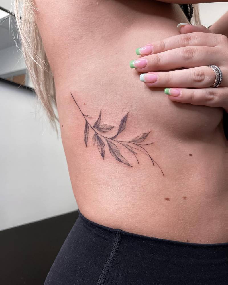 Leaves tattoo located on the side boob, illustrative style.