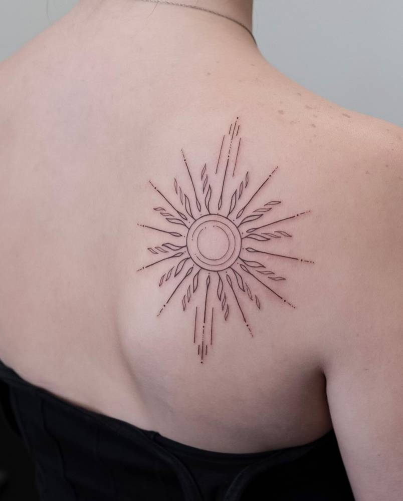 Ornamental sun tattoo located on the shoulder blade, fine line style.