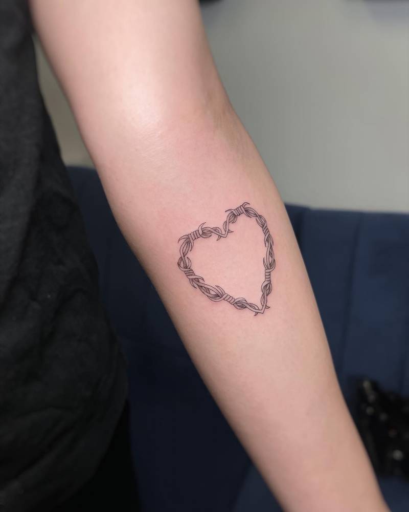 Fine line style barbed wire heart tattoo located on the inner forearm.
