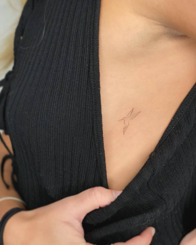 Fine line style hummingbird tattoo placed on the side boob.