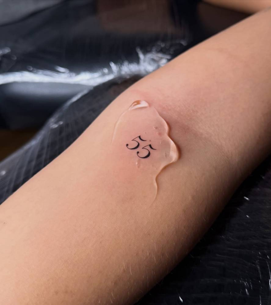 Lettering tattoo of the number "55" located on the inner forearm.
