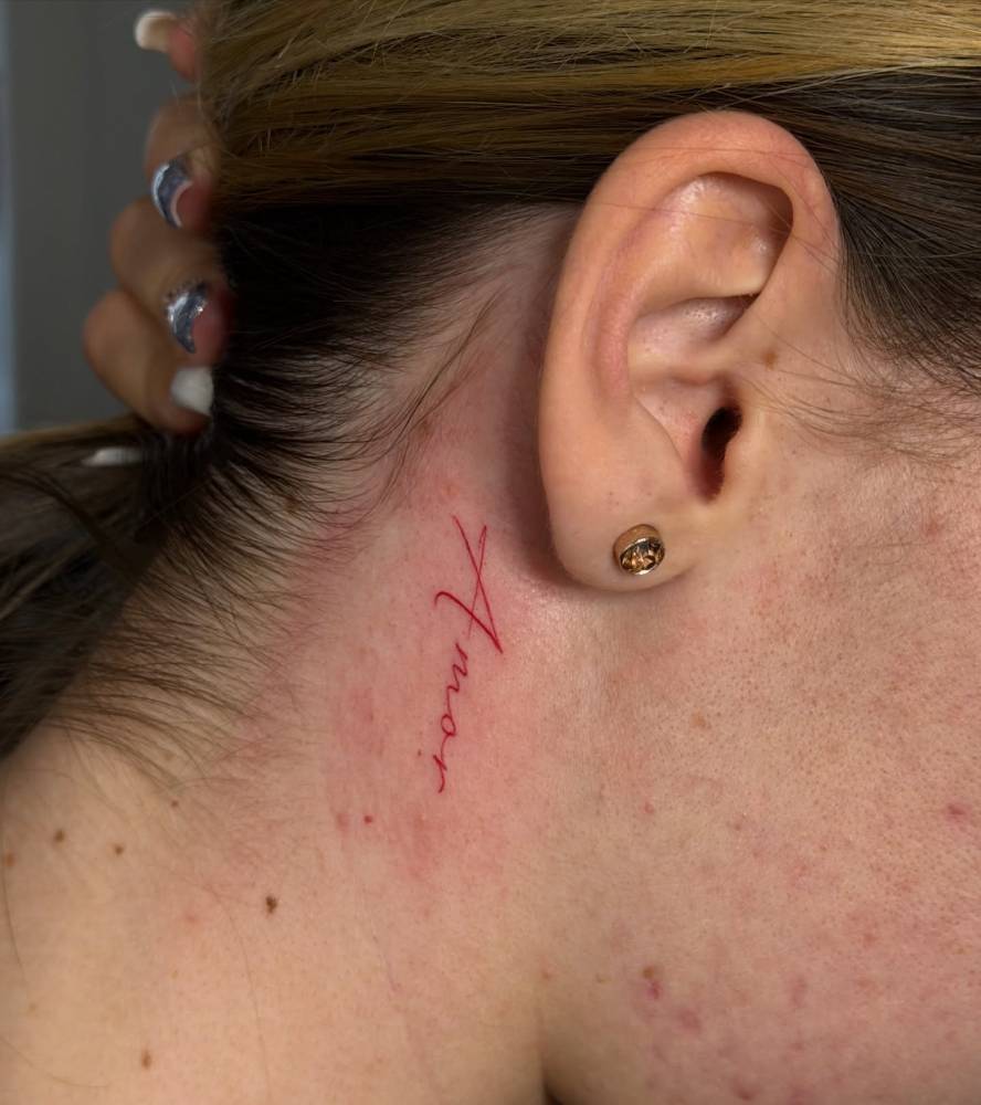 Word "amor" in red ink tattooed behind the ear.