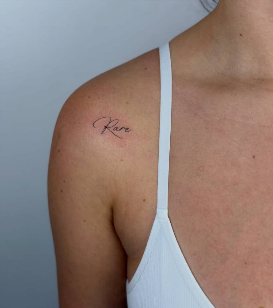Handwritten font word "rare" tattoo located on the shoulder.