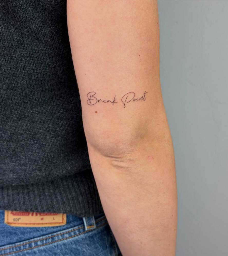 Lettering tattoo that says "break point" located on the tricep.