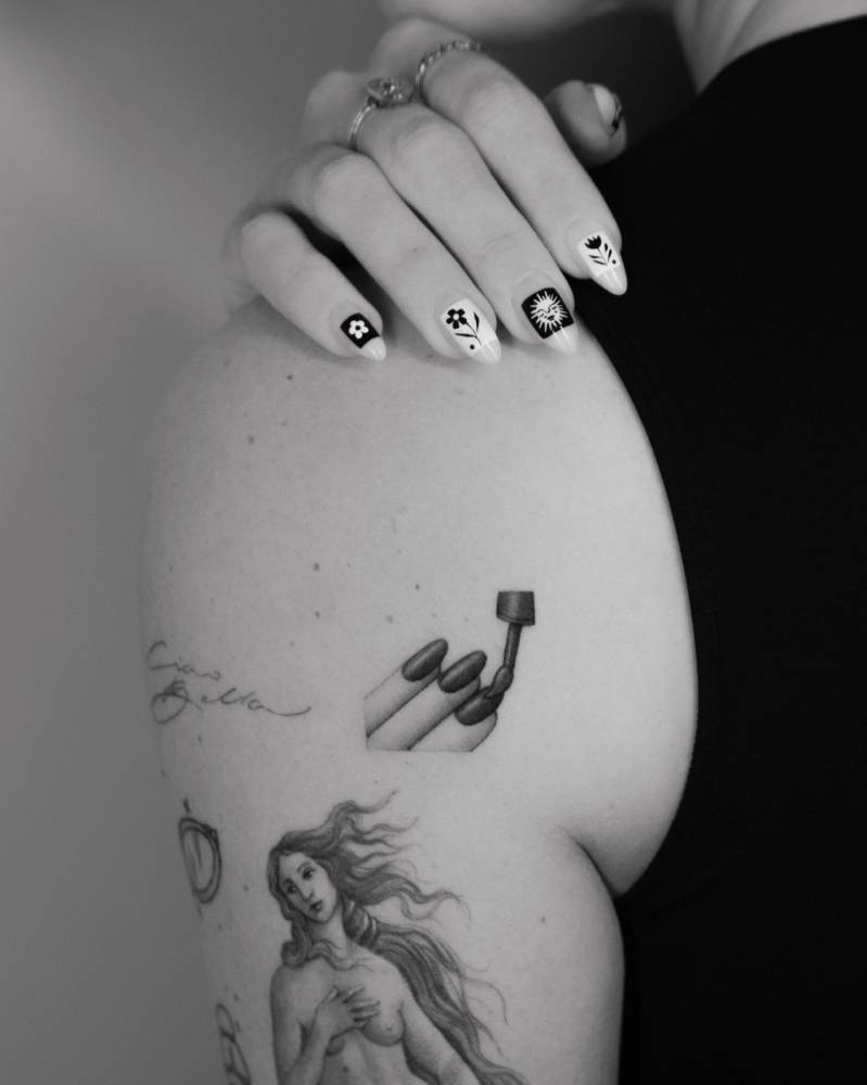 Nail polish tattoo located on the shoulder blade.