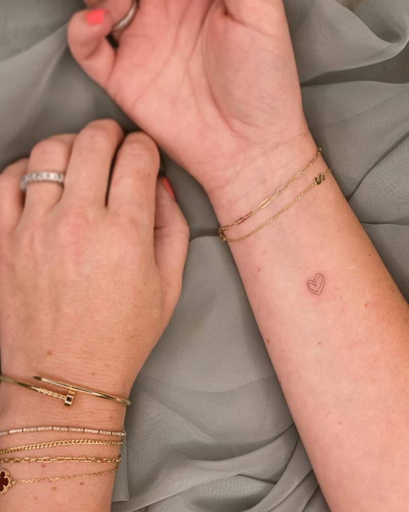 Fine line style heart tattoo located on the wrist.