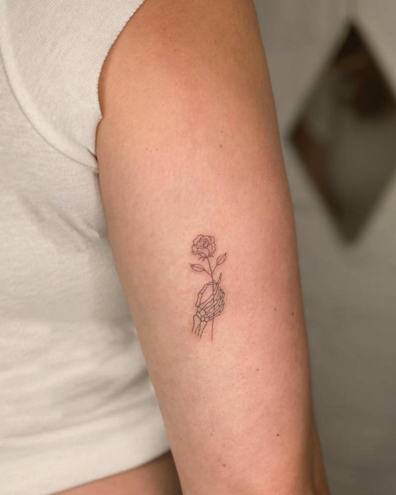 Skeleton hand holding flower tattooed on the tricep.