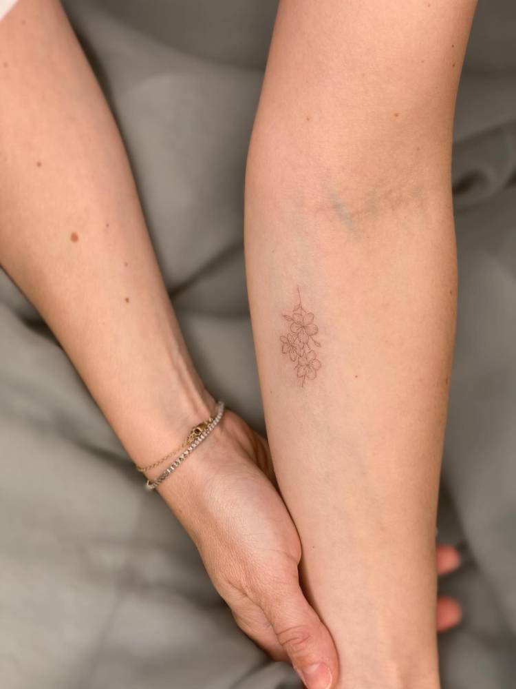 Almond blossom in fine line style tattooed on the inner forearm.