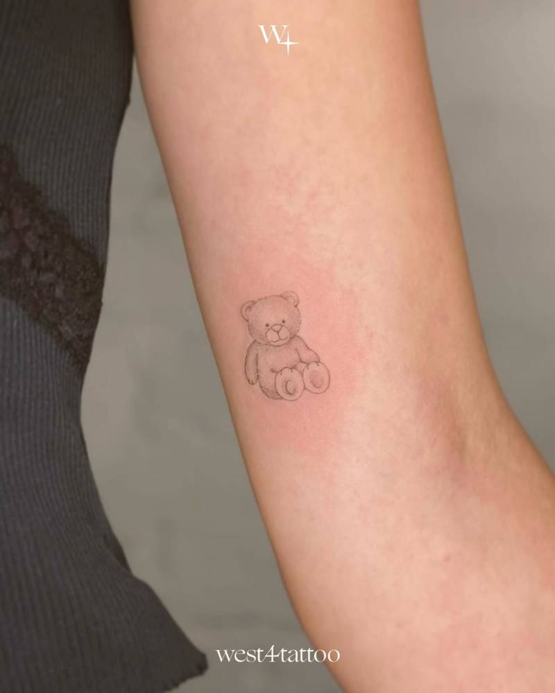 Teddy bear tattoo placed on the inner arm, illustrative style.