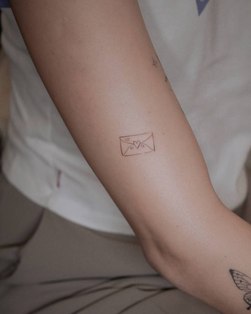 Fine line style love letter tattoo done on the upper arm.
