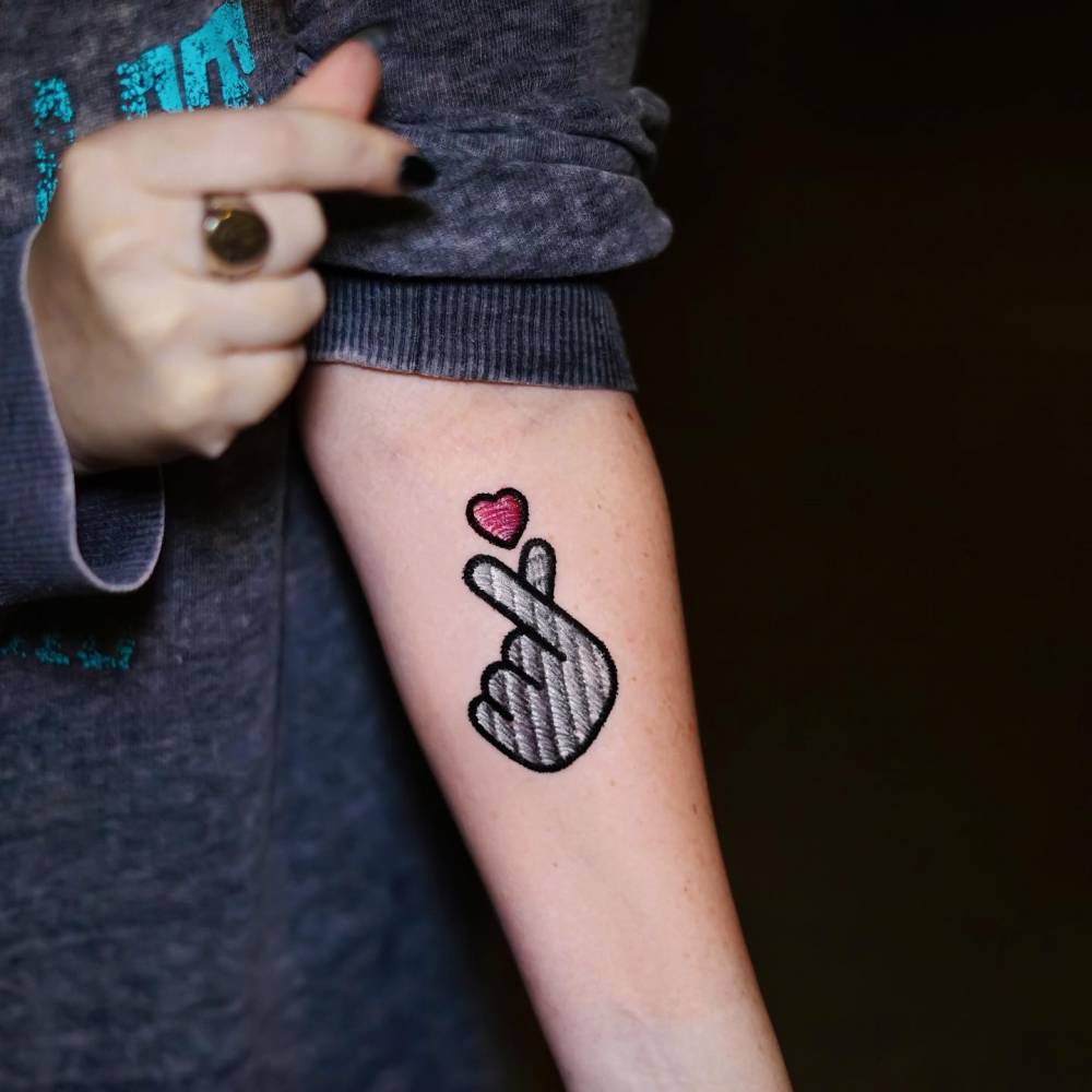 Embroidery style korean finger heart patch tattoo located on the inner forearm.