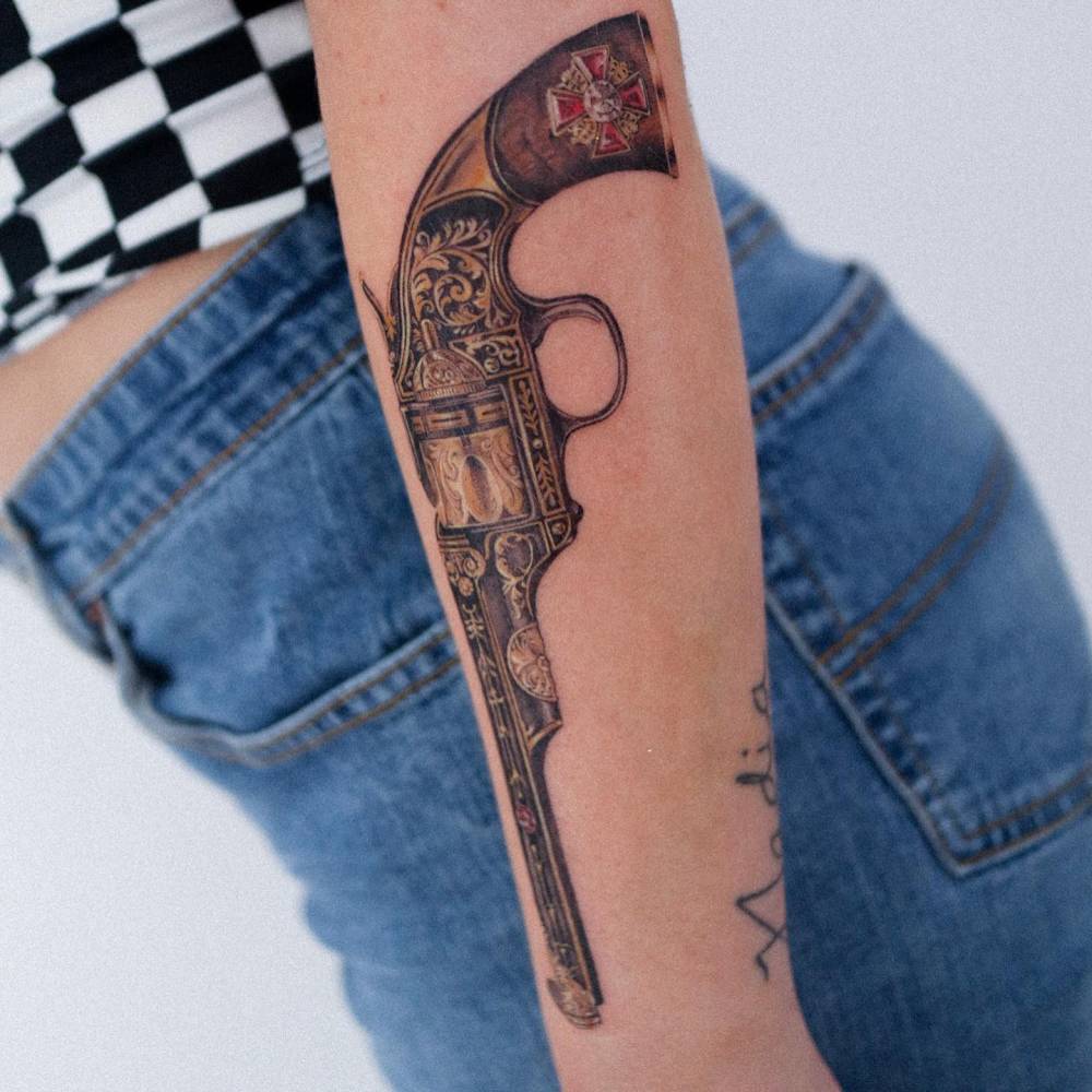Micro-realistic style revolver tattooed on the forearm.