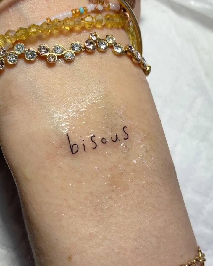 Lettering tattoo of the word "bisous" located on the wrist.