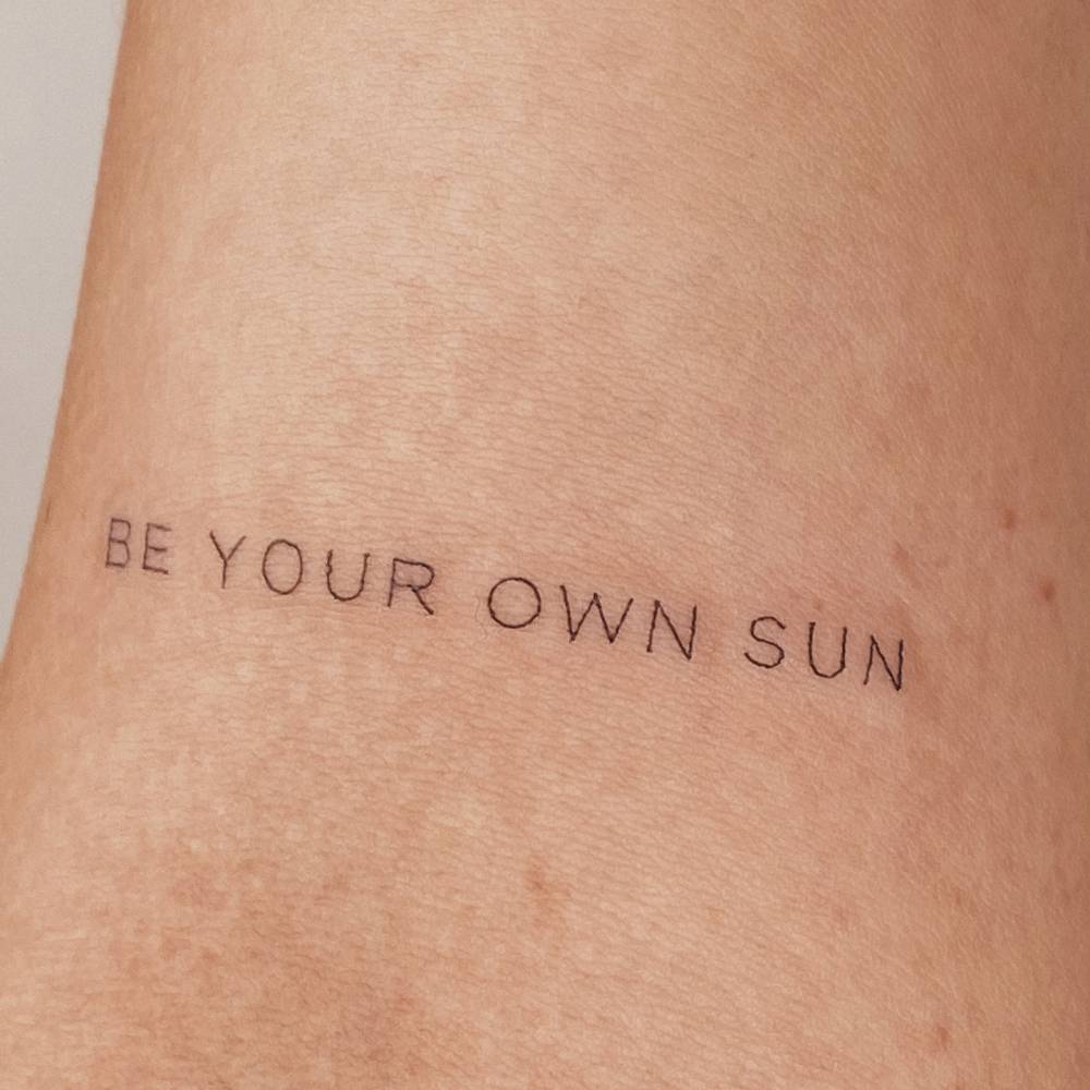 "Be your own sun" lettering tattoo located on the bicep.