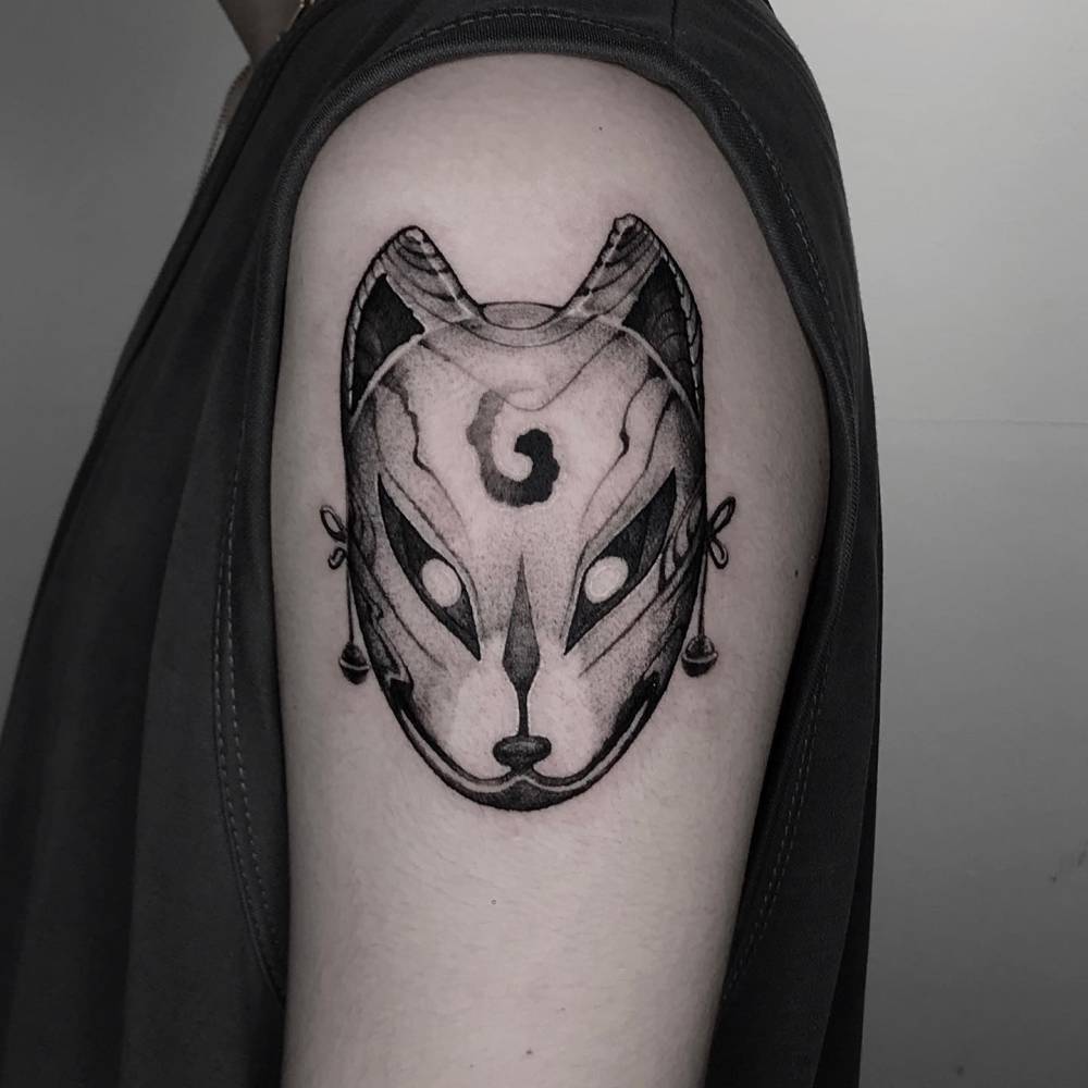 Kitsune mask tattoo in blackwork style located on the upper arm.