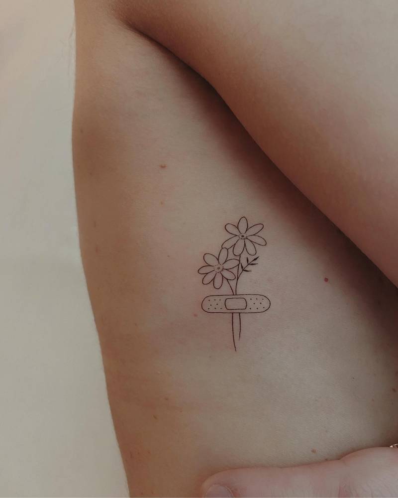 Bandage and flowers tattoo located on the rib, fine line style.