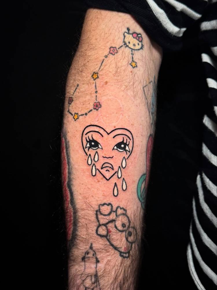 Cartoon style crying heart tattoo located on the forearm.